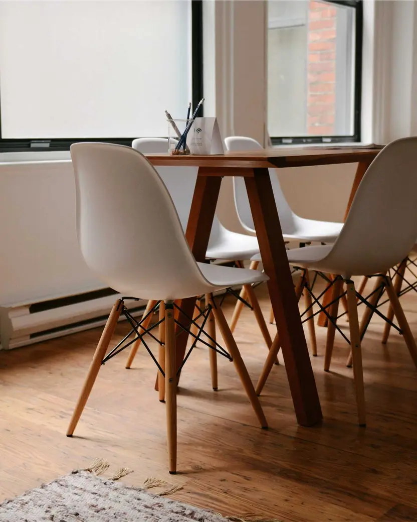 Comedor con mesa de madera, sillas blancas y grandes ventanales