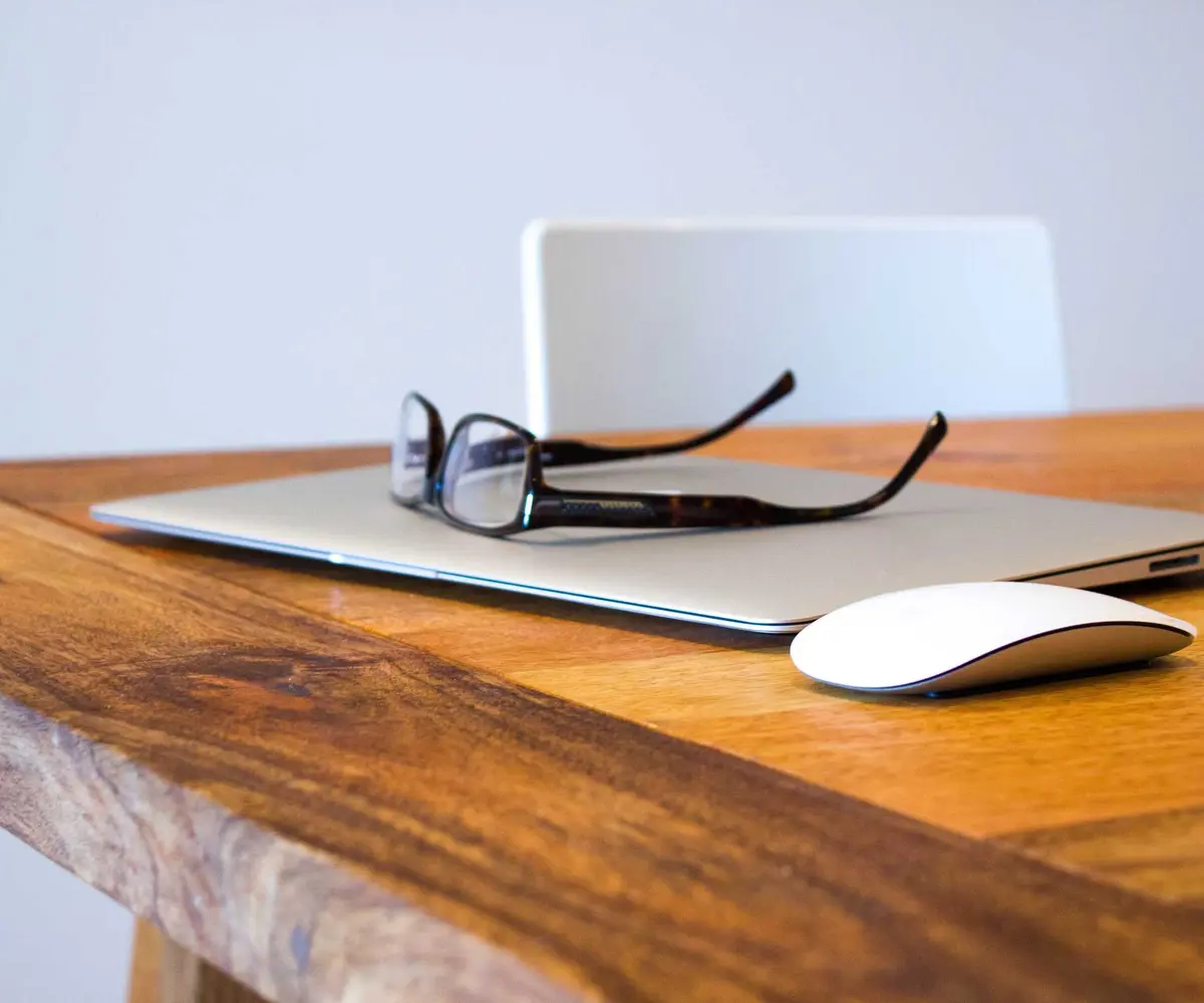 Portátil, gafas y ratón sobre un escritorio de madera
